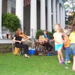 children dancing on the lawn while string instruments play in the background
