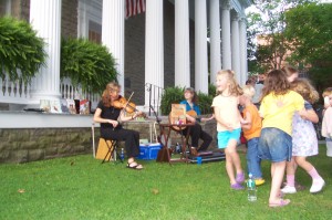 children dancing on the lawn while string instruments play in the background