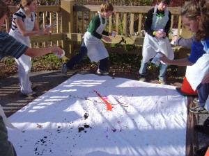 kids engaged in spatter painting a white tarp outside