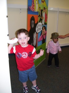 child trying a whisper tube with another child trying on a hat