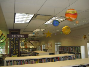 planets and stars hanging from the ceiling above book shelves
