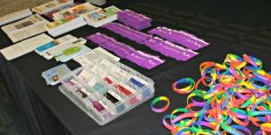 Brochures, ribbons, and rubber rainbow bracelets on a booth table.