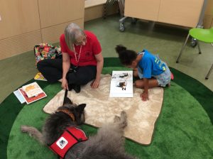 Photo of a child reading with a dog and adult