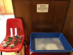 Dirty dinosaurs and sponges sitting beside a sensory tub of soapy water