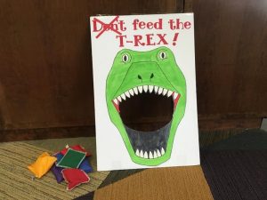 Picture of “Don’t Feed the T-Rex” bean bag toss. An image of a green dinosaur with a hole where his mouth would be, with bean bags sitting to the side