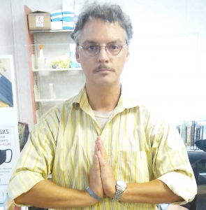 male librarian wearing glasses and yellow shirt with hands placed in namaste pose