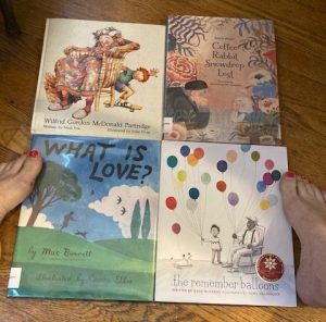 4 picture books that deal with children's relationship with people who have dementia. From left, first row: Wilfred Gordon McDonald Partridge; Coffee Rabbit Snowdrop Lost; 2nd row: What is Love; The Remember Baloons. Author's feet with ragged pink nail polish show up on either side of the books.
