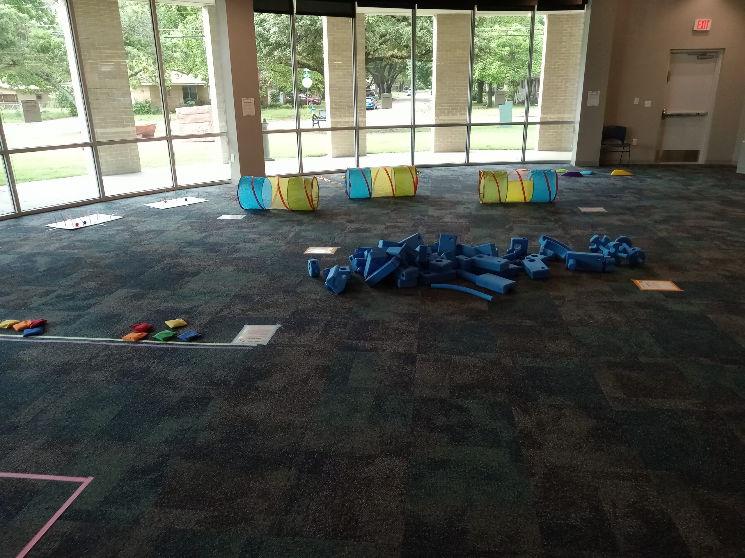 Library program room set up for Toddler Games with bean bags, blocks, crawling tunnels, and balancing stones