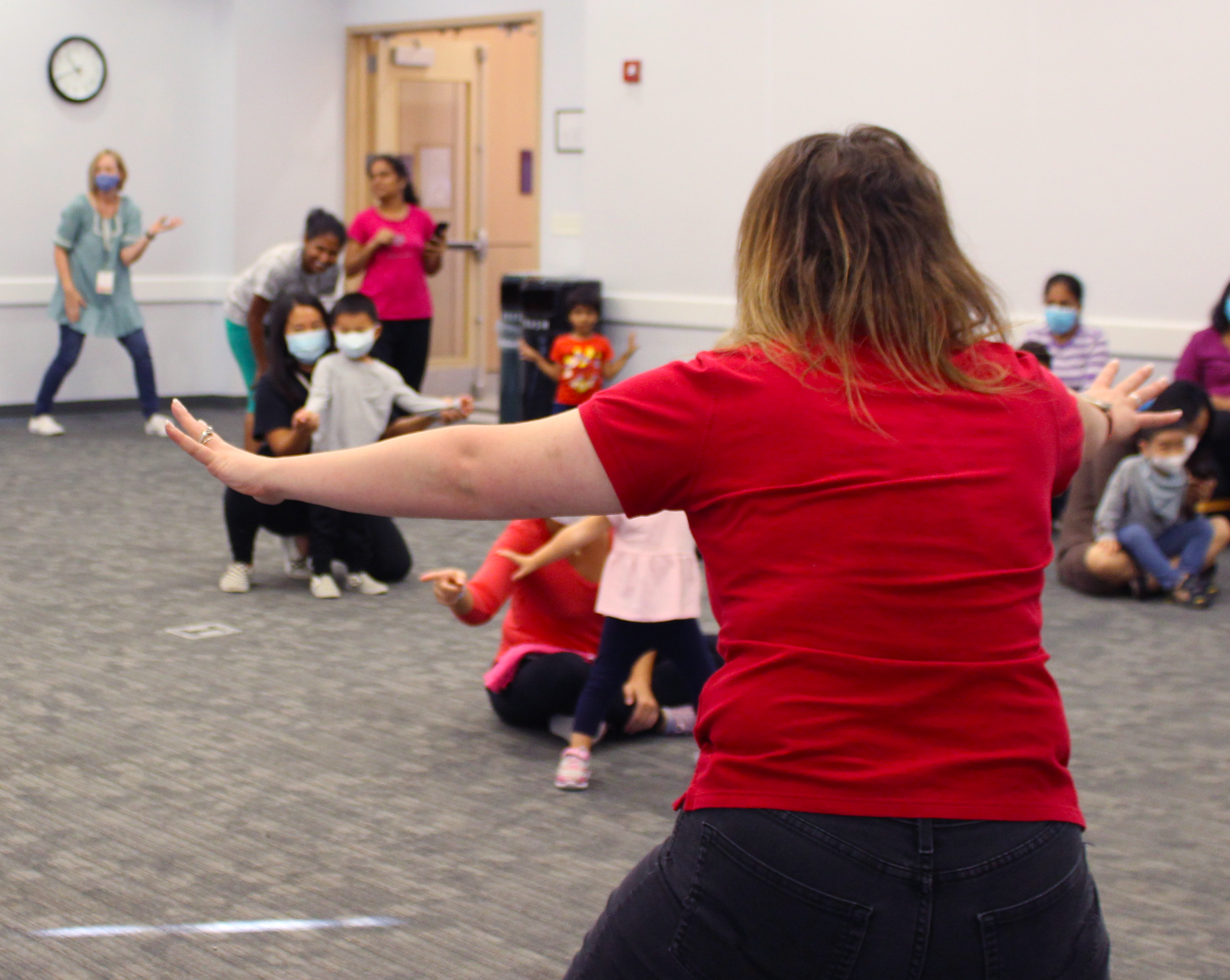 A staff member demonstrates a dance at the front of room of children.