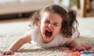 A child cries and yells laying on her stomach on the floor