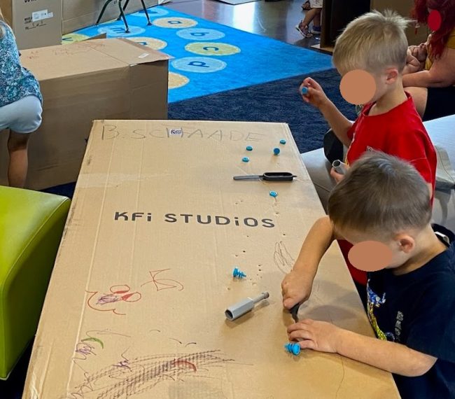 Two young children using screwdrivers on cardboard.