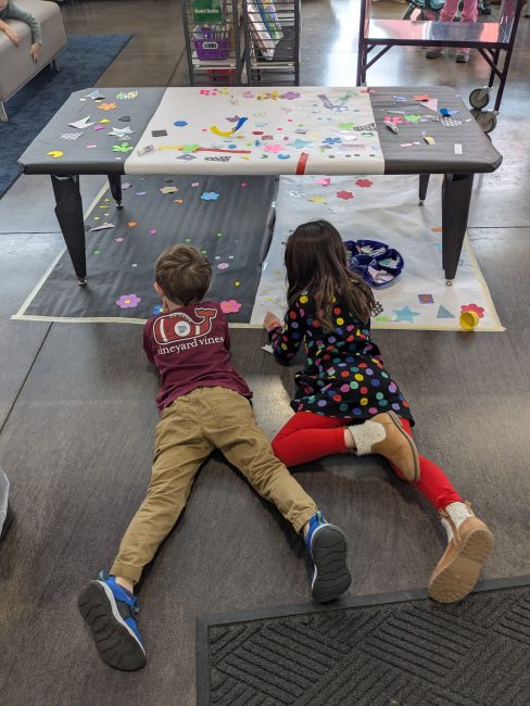 Two children lying on their stomachs on the floor creating art.