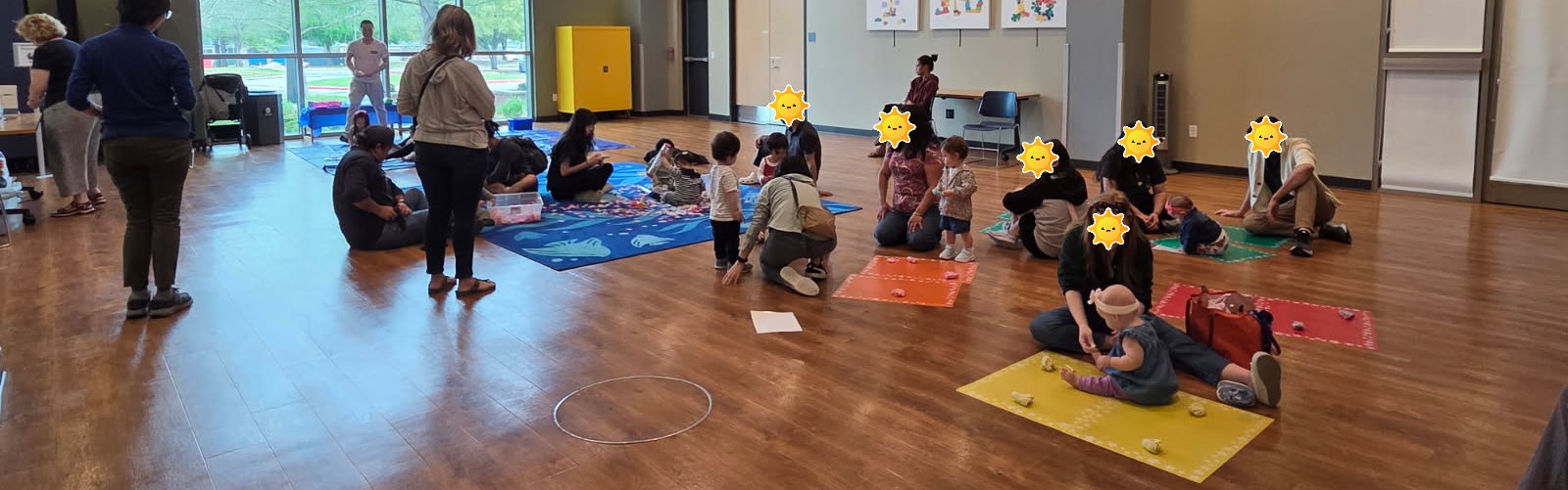 A room full of children and adults engage with nature-based play activities include scented dough, flower petals, and sensory tubes.