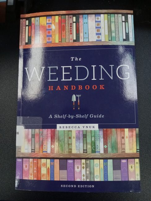 The book "The Weeding Handbook: A Shelf-by-Shelf Guide" by Rebecca Vnuk sits on a desk.