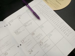 A calendar sits open to a spread of dates. Text is written on several dates, with a to-do list on the right side of the page.