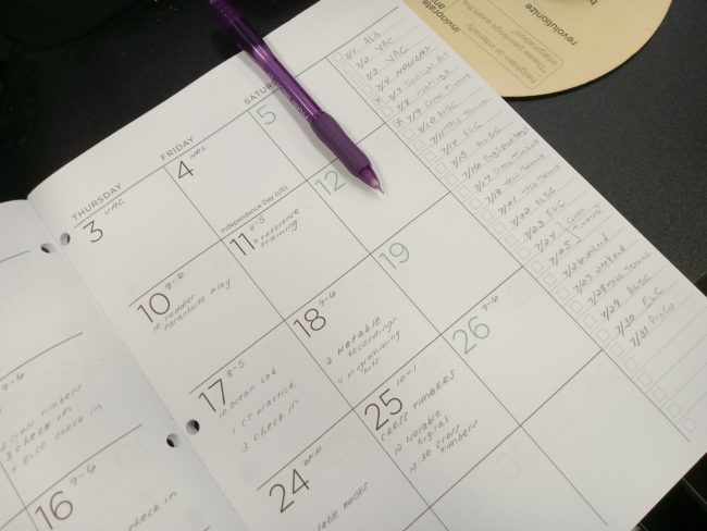 A calendar sits open to a spread of dates. Text is written on several dates, with a to-do list on the right side of the page.
