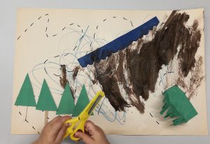 A child holding a pair of yellow scissors over a raft of a map the child created.