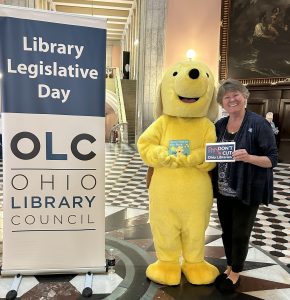 Maria Simon, Youth Services Coordinator for Wood County Public Library, stands next to a yellow dog mascot