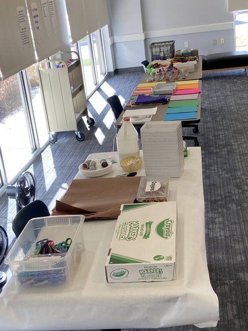 A row of tables hold craft supplies like scissors, markers, glue, paper, and more.