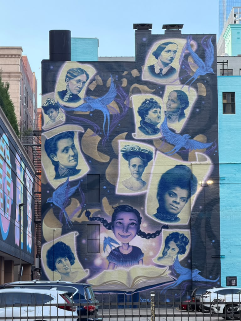 Street mural with a girl reading a book and historic women all around her