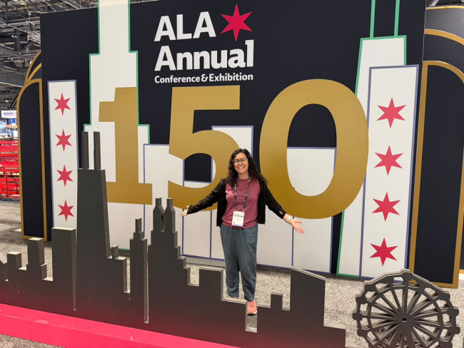 The author (Gabi Silva) standing with her arms open in front of a sign that says "ALA Annual Conference & Exhibition"