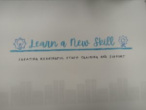 Blue text reads Learn a New Skill. Under a blue line, the additional text Creating Meaningful Staff Training and Support appears in black. To the left of the text is the outline of a lightbulb inside a gear. To the right of the text is the outline of a gear with tools.